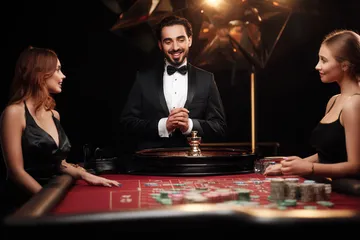 A professional dealer in a tuxedo greeting players at the roulette table, symbolizing the authentic live casino feel at 83JLPH.